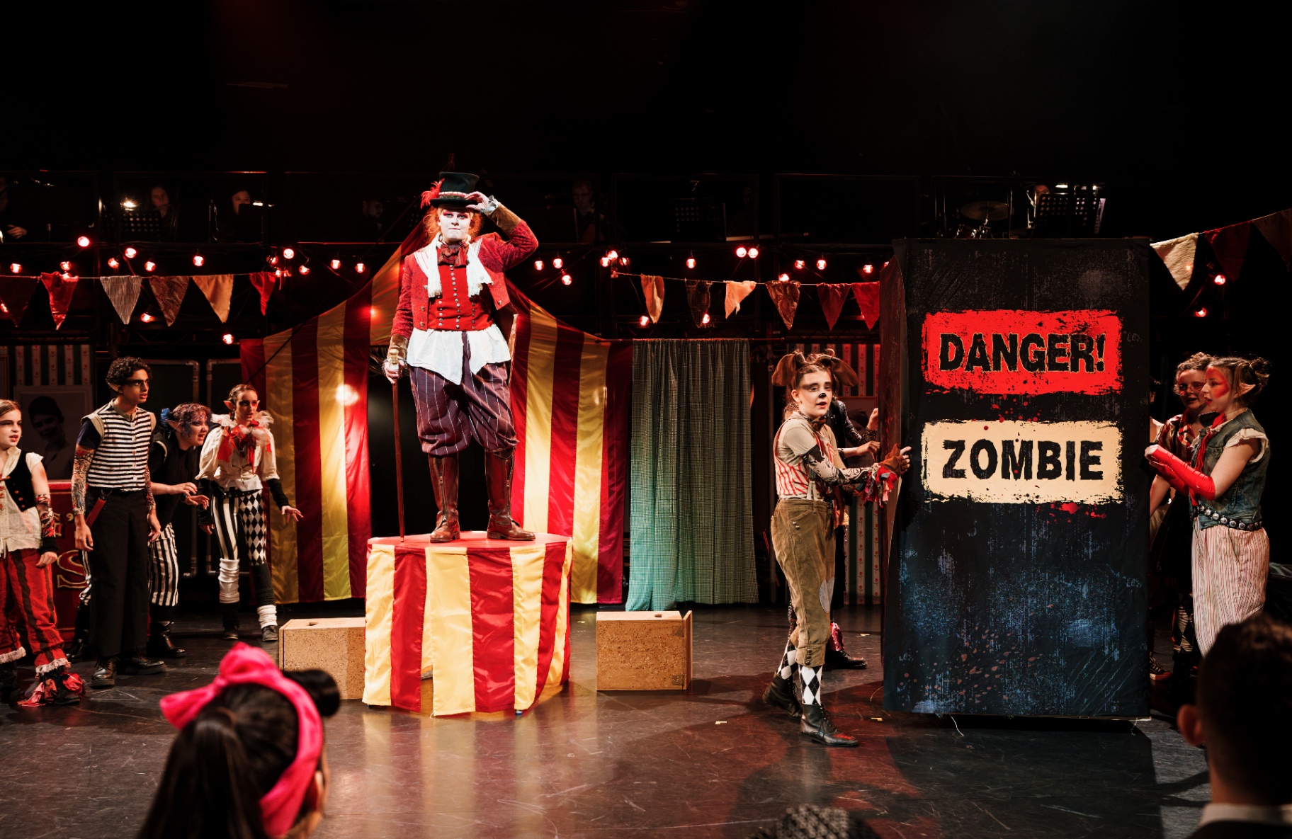 The Ringmaster stands atop a striped podium beside a 'Danger! Zombie' sign.