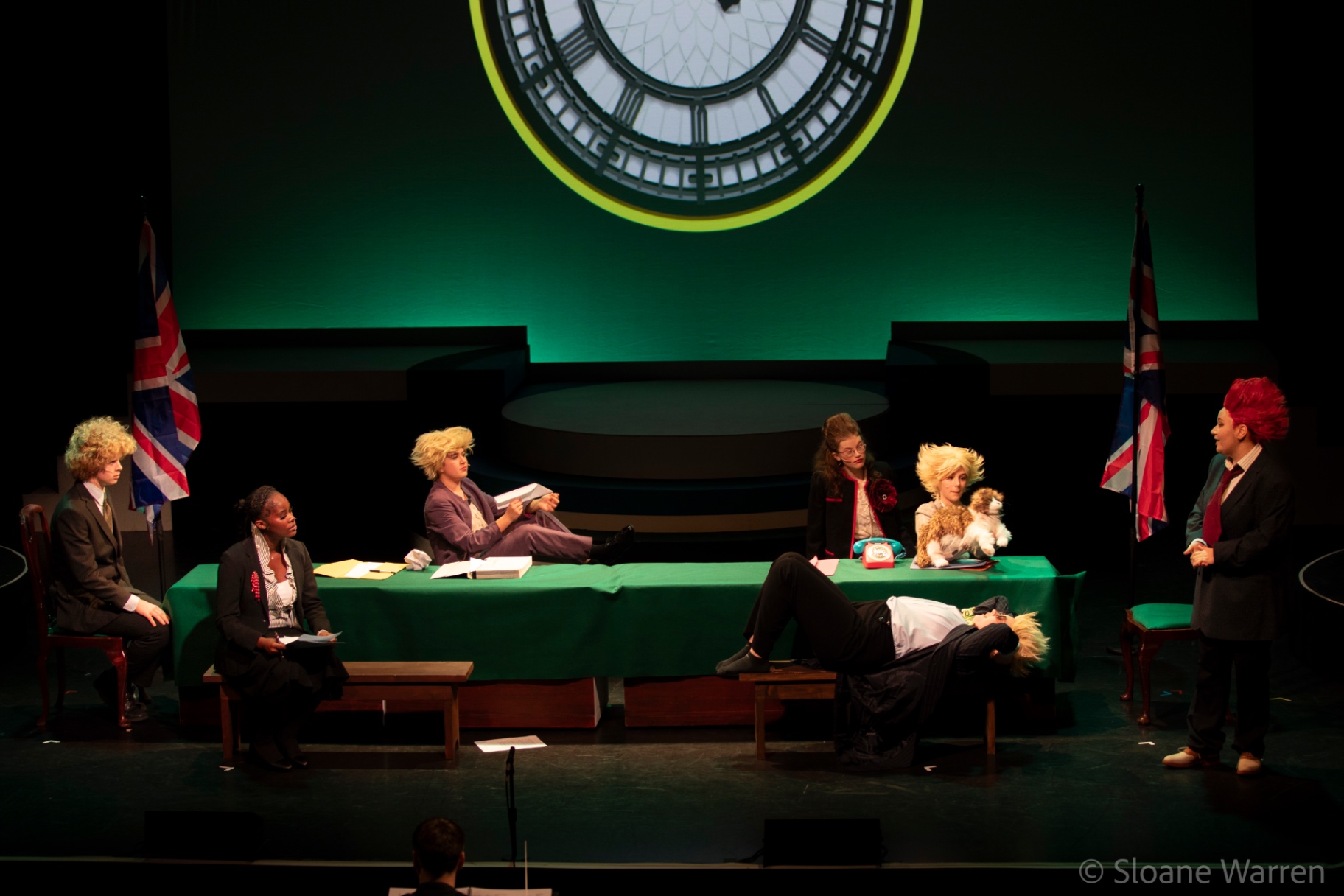 A satirical Cabinet meeting: ministers slouch and doze around a green baize table beneath the illuminated face of Big Ben, flanked by Union flags.