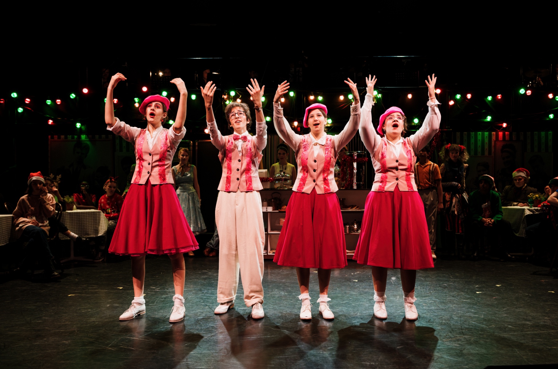 Four performers in pink berets and red skirts dance in unison.